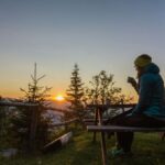 Woman having coffee outdoors early in the morning, looking at the sunrise.