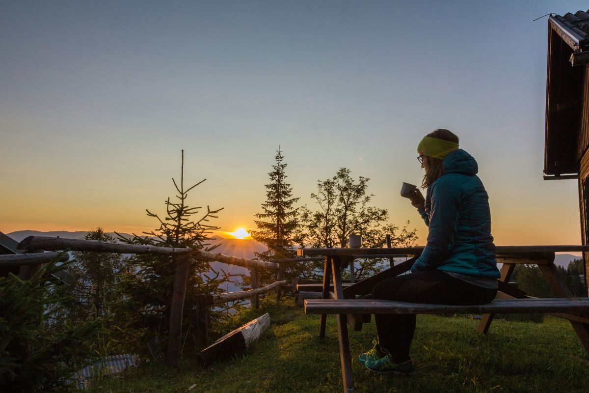 Woman having coffee outdoors early in the morning, looking at the sunrise.