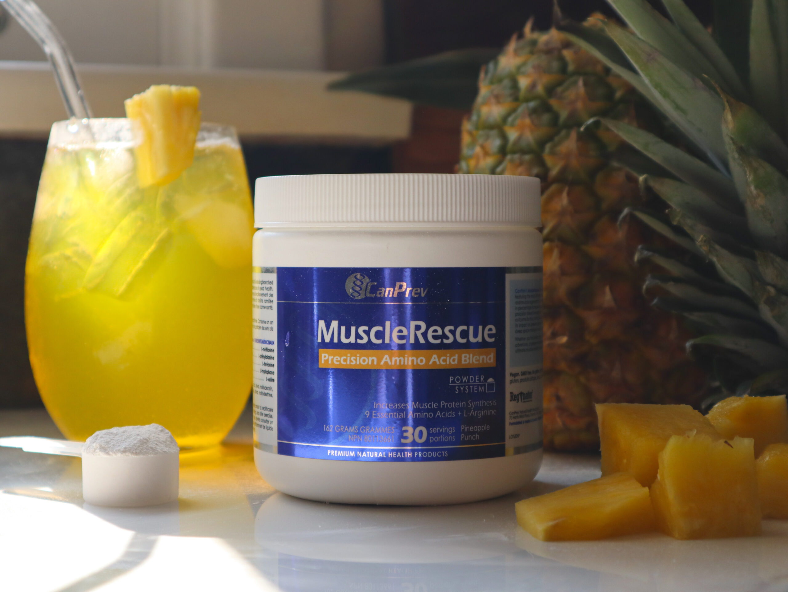 CanPrev's MuscleRescue bottle beside a pineapple and a glass of MuscleRescue mixed in water